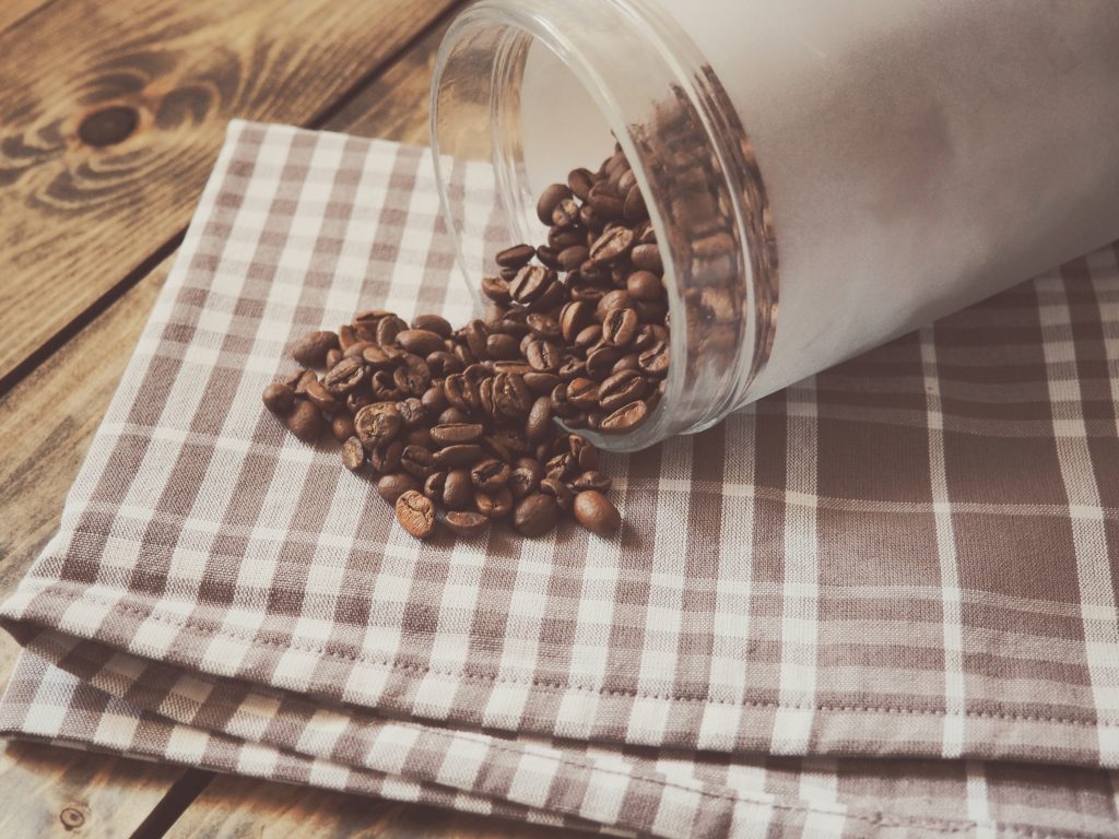 Coffe Beans in glass jar spilling out onto dishcloth
